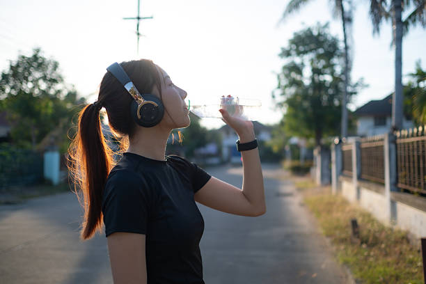istock A woman is drinking water while wearing headphones 2227553649