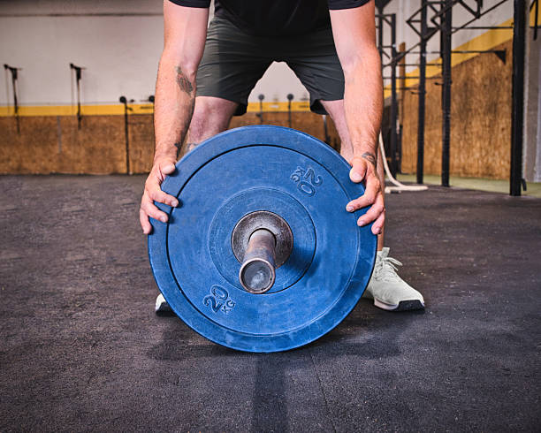 Focused adult man lifting a heavy blue barbell overhead during an intense workout in a cross training gym. Fitness and strength training concept with determination and athletic effort.