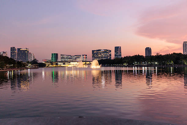 The breathtaking skyline of Bangkok glows softly during twilight, mirrored perfectly in the calm waters of the Chao Phraya River. The warm hues of the setting sun blend with city lights, creating a serene and captivating urban reflection.