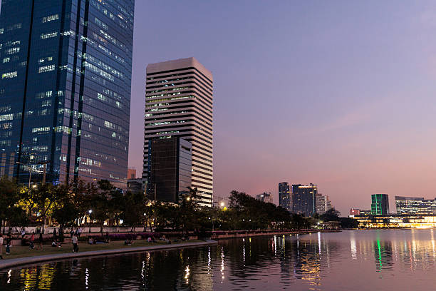 The stunning skyscrapers of Bangkok stand tall against the vibrant hues of twilight. The soft, warm colors of the sunset blend with the city lights beginning to glow.