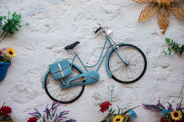 istock Art installation on a white concrete wall with a vintage bicycle surrounded by artificial flowers. 2227556015