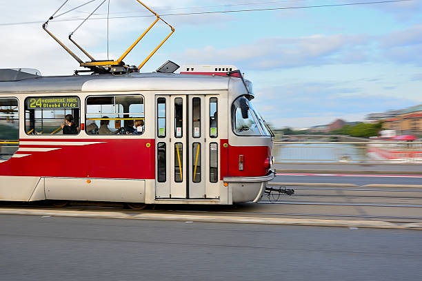 Red and white tram navigating over a bridge in prague, with the picturesque vltava river flowing in the background on a sunny day