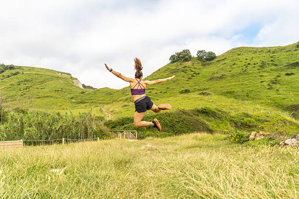 Woman energetically jumps in the lush green hills of zumaia, gipuzkoa, showcasing the natural beauty of the basque country's flysch coastline