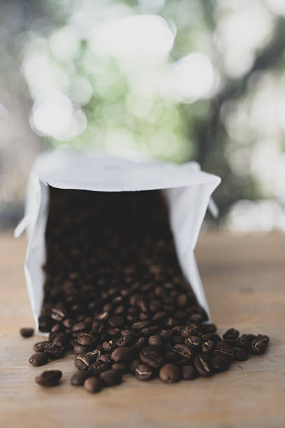Paper coffee bag packaging on a wooden surface alongside scattered coffee beans