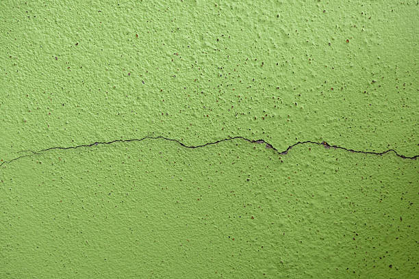 Weathered building wall with thin cracks. Dark spot holes highly visible on the green painted surface. Shows decay, damage, and urban texture. Ideal for architectural and grunge themes.