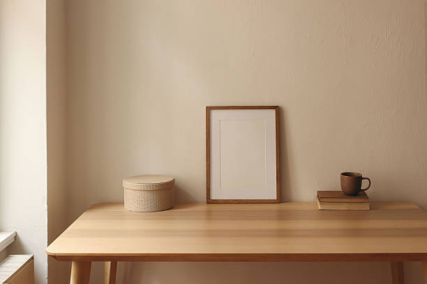 istock Wooden vertical picture frame, poster mockup on table. Minimalist home interior. Coffee cup, books, round storage box against beige wall background. Cozy natural workspace. Reading corner, warm tones. 2227560966