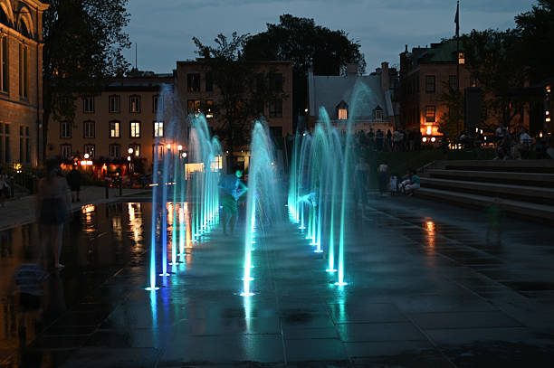 Kids playing in water fountain stream at the  City Hall public park in Quebec city during summer evening