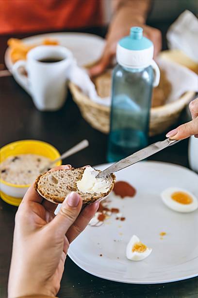 istock Close-up of hands spreading cream cheese on whole grain bread at breakfast, with eggs, coffee, and water bottle on the table. Cozy morning meal setting 2227568164