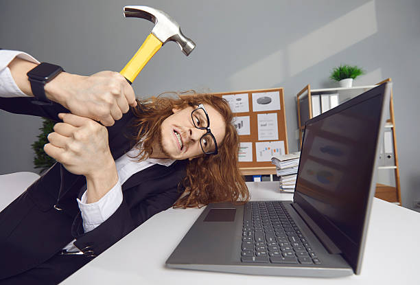 istock Funny young office worker sitting in office feeling ready to hit computer with hammer 2227569249
