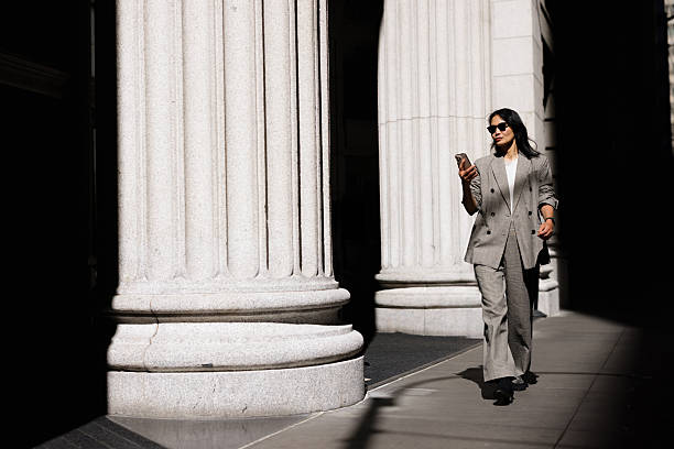 istock Businesswoman walking and using smartphone near columns 2227571921