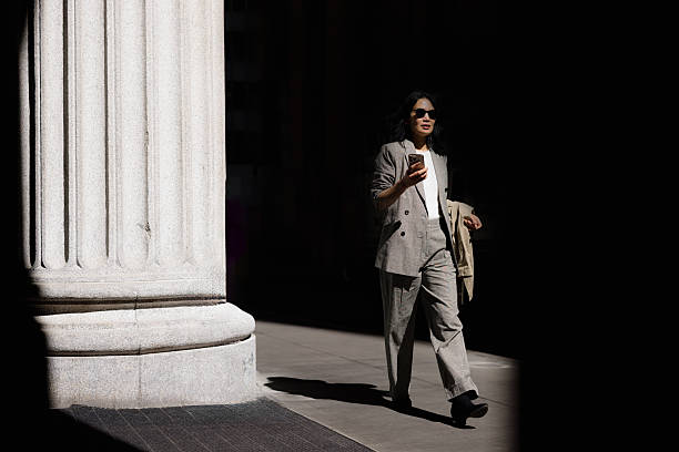 istock Businesswoman walking and using smartphone near marble column 2227571944
