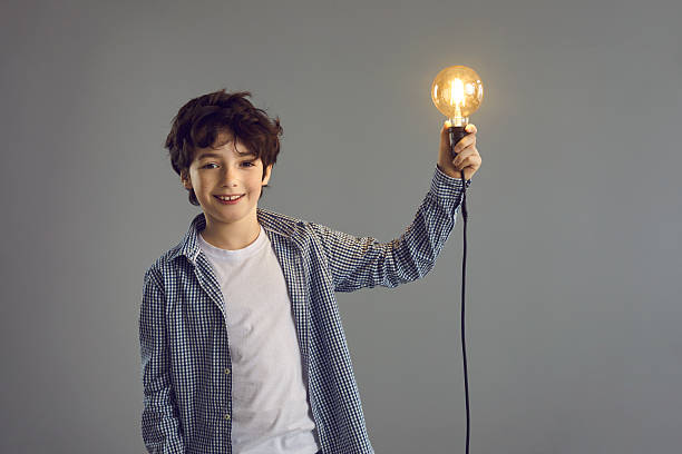 istock Boy holding glowing light bulb lamp standing isolated on grey studio copy space 2227573278