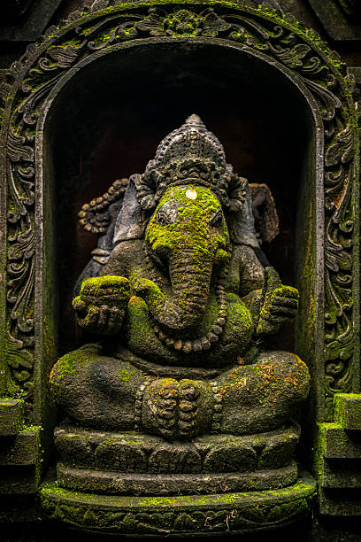 An old hindu stone statue of Ganesha covered with moss, standing on the street on the Bali island in indonesia