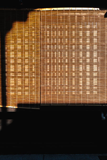 Sunlight filtering through traditional japanese bamboo blinds, creating a textured effect on a building exterior