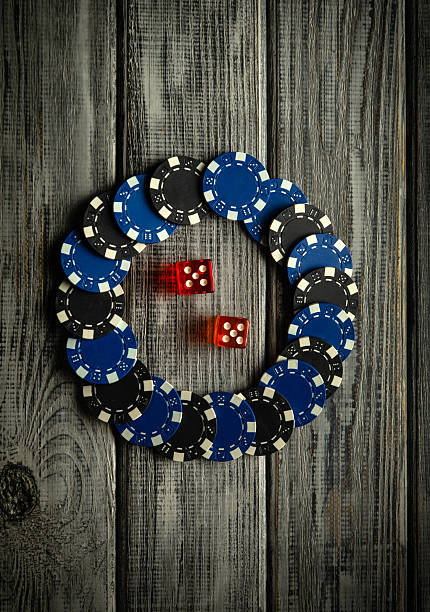 istock Poker chips in black and blue create a circular arrangement on a rustic wooden table, accompanied by two vibrant red dice, suggesting a game night atmosphere 2227580998