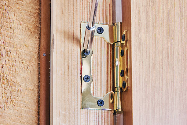 istock Carpenter installing complete door hinge onto wooden door edge, securing metal hinge with screws, detailed view of installation process shown. 2227582533