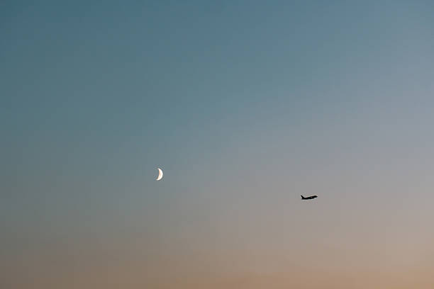 A serene twilight sky with a crescent moon glowing softly and an airplane soaring in the distance. The gradient of warm and cool tones creates a peaceful and dreamy atmosphere, symbolizing travel and freedom.