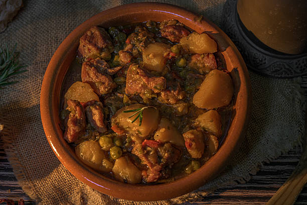 Traditional autumn beef stew with potatoes and peas in a rustic clay bowl. Warm cozy setting with pinecones, bread and natural textures. Seasonal homemade comfort food