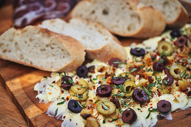 A beautifully styled butter board featuring a spread of creamy butter, garnished with green and black olives, fresh herbs, and spices