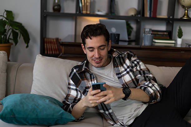 istock Young man is using mobile phone while relaxing on sofa at home 2227585315