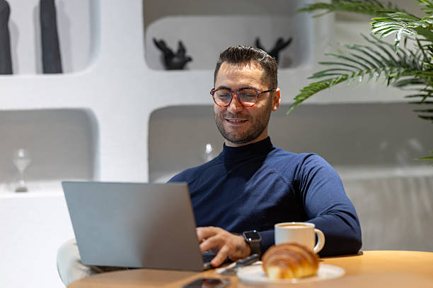 istock Young businessman working on laptop while having a croissant and coffee for breakfast in modern office 2227593748