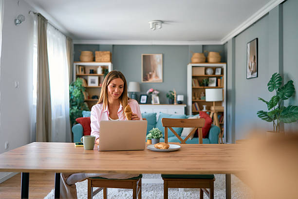 istock Woman eating breakfast and working from home using laptop 2227594796
