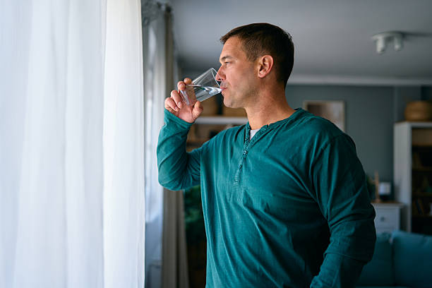 istock Man drinking water looking out the window in the morning 2227594981
