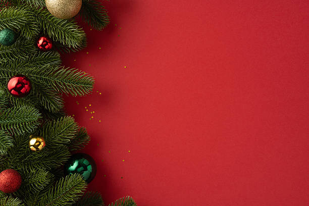 istock Green pine branches with colorful baubles on a red backdrop representing Christmas festivity 2227600315