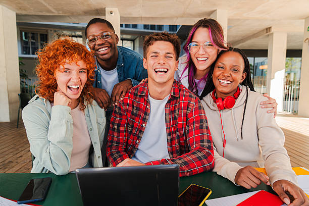 istock Smiling multiracial group of young students looking at camera, sitting together in university library with a laptop, books, and notebooks. Diverse classmates studying and collaborating at university 2227602021