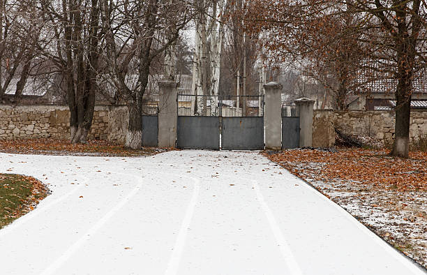 istock A snow-covered path leads to a closed gate surrounded by bare trees and fallen leaves. 2227602687