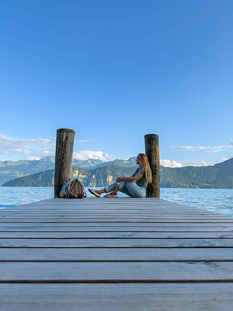 istock Woman Sitting on Pier by Mountain Lake 2227604301