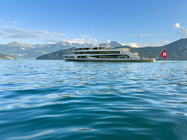 Large white passenger ferry cruising on calm blue lake with mountainous landscape in the background. Scenic boat on water with clear sky and distant hills. Travel and transportation concept.