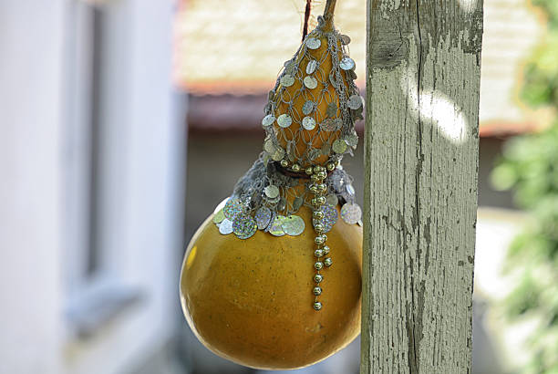 A decorative gourd, painted yellow and adorned with beads, hanging on a wooden surface