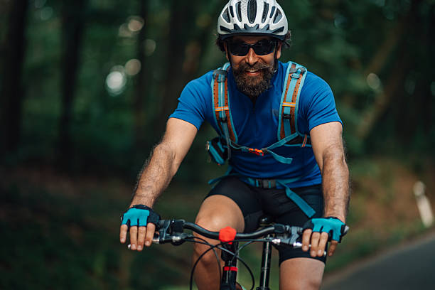 Male cyclist wearing a helmet and hydration pack smiles while riding his mountain bike on a forest trail