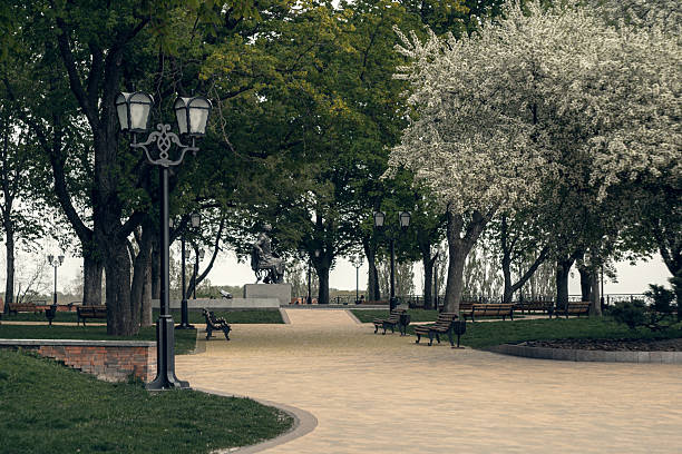 A tranquil park scene featuring a curving path, vintage lanterns, and blooming spring trees. The inviting benches and shaded walkway evoke calm and relaxation in a natural urban setting.