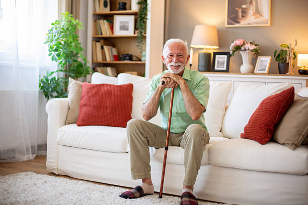 istock Senior man sitting on sofa holding walking cane smiling at camera 2227611546