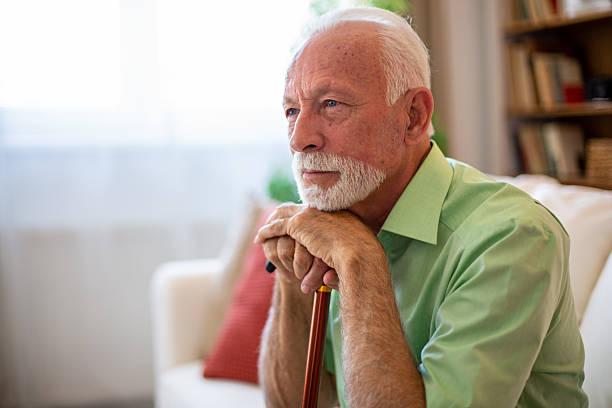 istock Senior man sitting on sofa leaning on walking cane contemplating life 2227611563