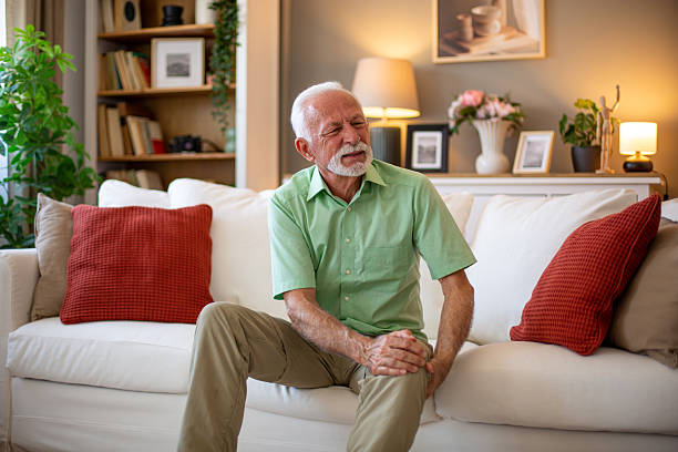 istock Senior man experiencing knee pain while sitting on sofa at home 2227611611