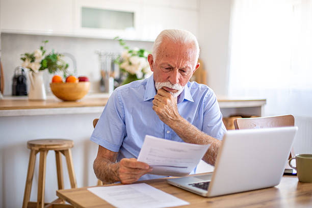 istock Worried senior man reading documents and using laptop at home 2227611977