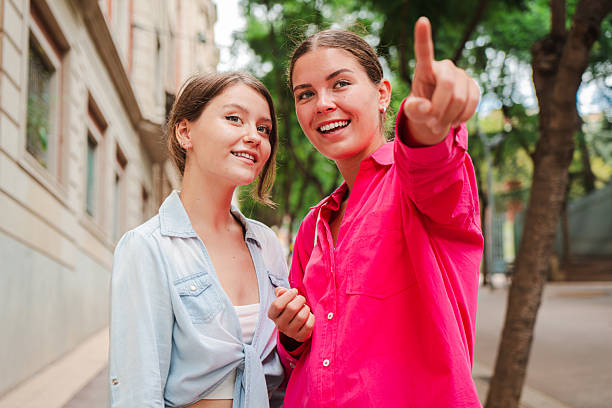 istock Two young women pointing forward, enjoying a moment together outdoors, smiling and engaged, in a city setting on a casual day, sharing excitement and curiosity about their surroundings. 2227614420