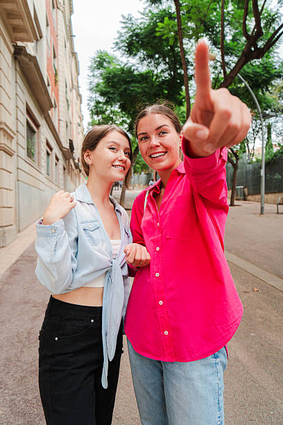 istock Vertical. Two young women pointing forward, enjoying a moment together outdoors, smiling and engaged, in a city setting on a casual day, sharing excitement and curiosity about their surroundings. 2227614852