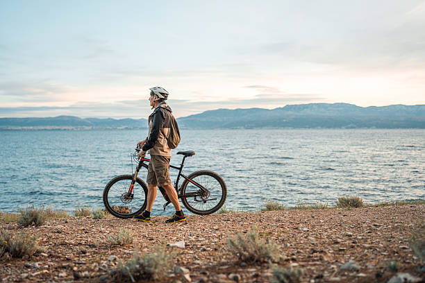 A smiling mature Caucasian man stands beside his electric mountain bike, enjoying the scenic Adriatic Sea backdrop.