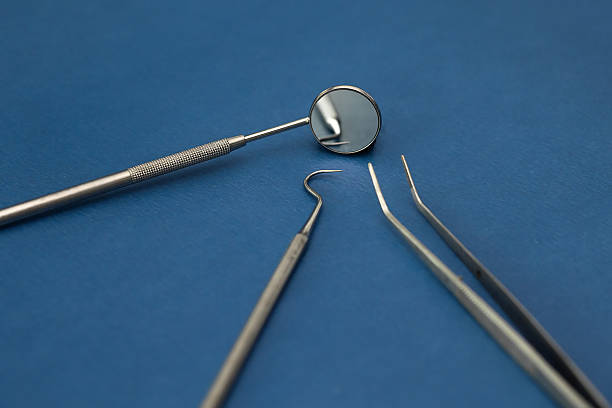 Close-up of a stainless steel dental tool on solid blue background. Sterile professional equipment used for precision procedures in modern restorative dentistry.