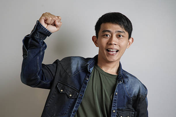 Excited Asian Man Celebrating with Raised Fist, An excited young Asian man with a wide smile raises his fist in celebration