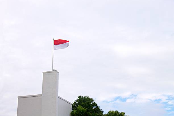 istock Indonesian Flag Waving on Rooftop Against Bright Cloudy Sky 2227625415