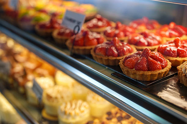 Close-up of vibrant strawberry tarts arranged neatly inside a bakery glass display case under soft lighting.