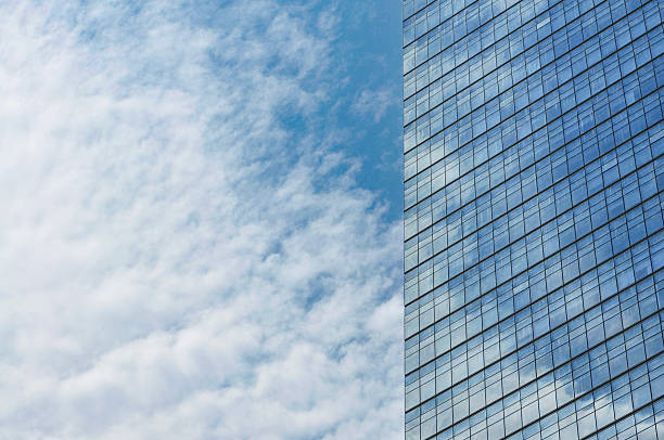 Glass mirror skyscraper wall with blue sky and white clouds reflection close up