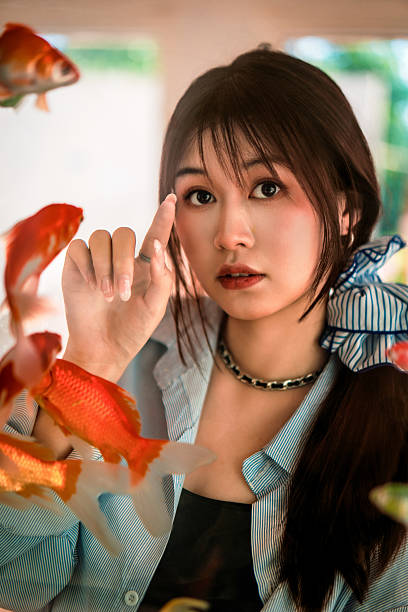 Young woman looking at goldfish in fish tank with curious expression.