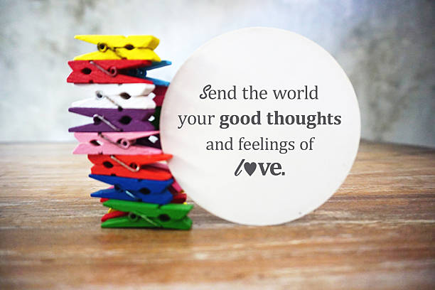 Inspirational quote - Send the world your good thoughts and feelings of love. Motivational text on white circle paper with colorful pile of clothespins holding notepaper illustration on a wooden table