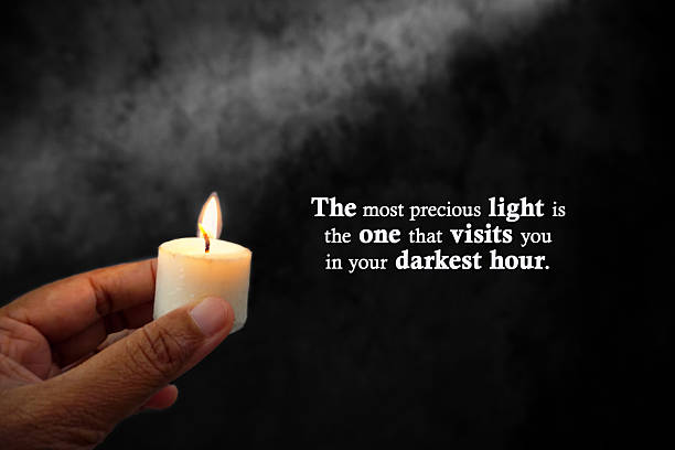 Inspirational motivational quote - The most precious light is the one that visits you in your darkest hour. With person holding candle light in the dark on black art abstract background. Kindness.